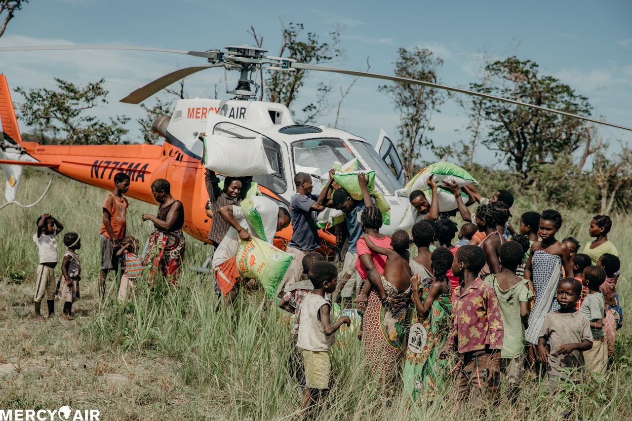 Mercy Air crew unloading aid sacks to a crowd beside the N775MA helicopter