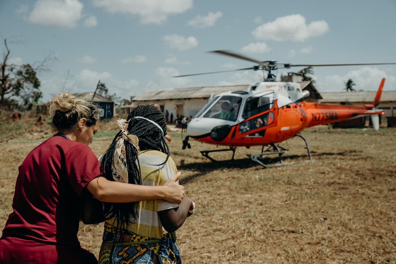 Aid worker comforting a woman beside the Mercy Air helicopter