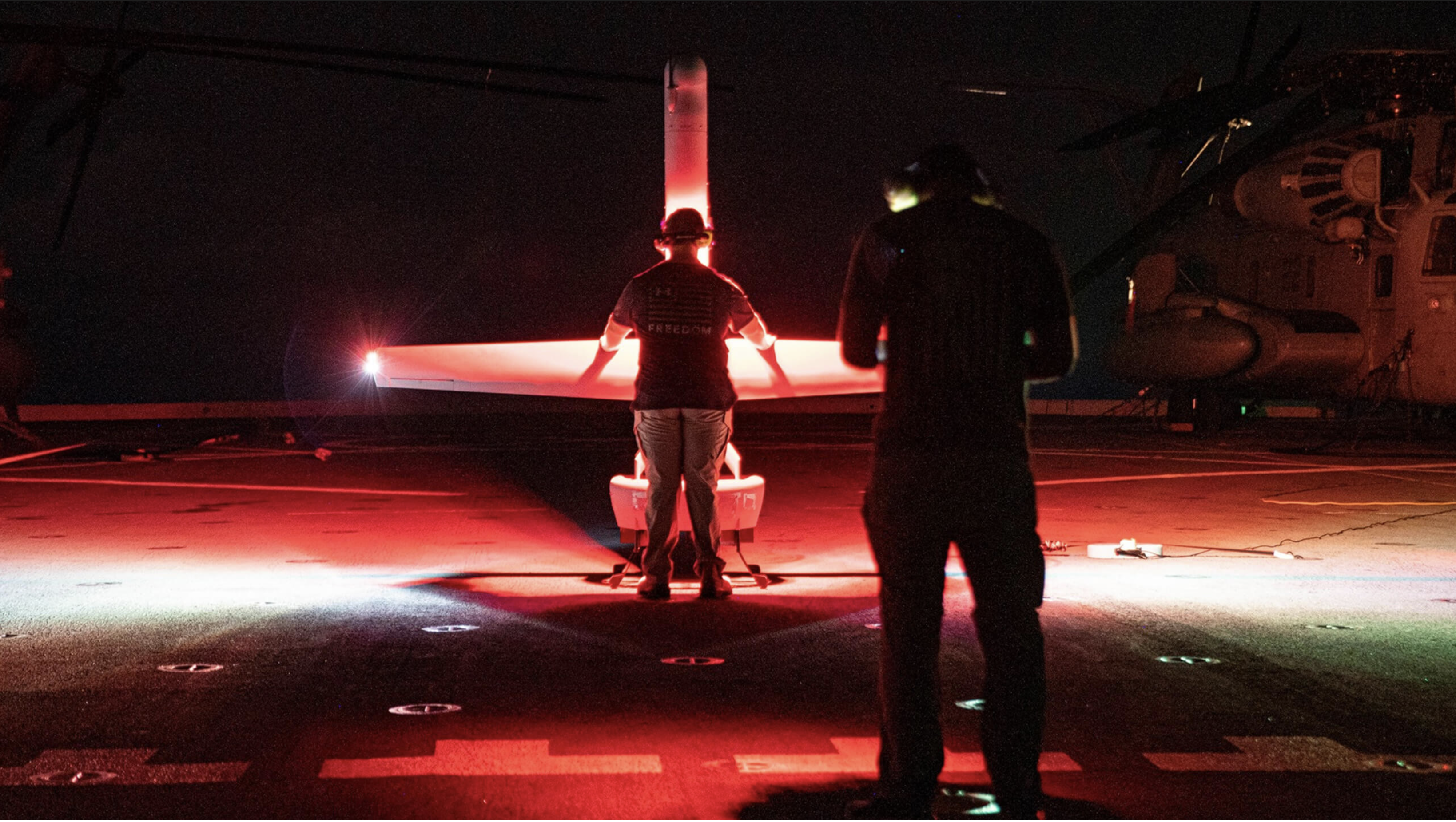 UAV lit at night on a ship deck during launch ops